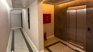 Un couloir moderne avec un sol en marbre, un panneau rouge indiquant la sortie de secours et un ascenseur.