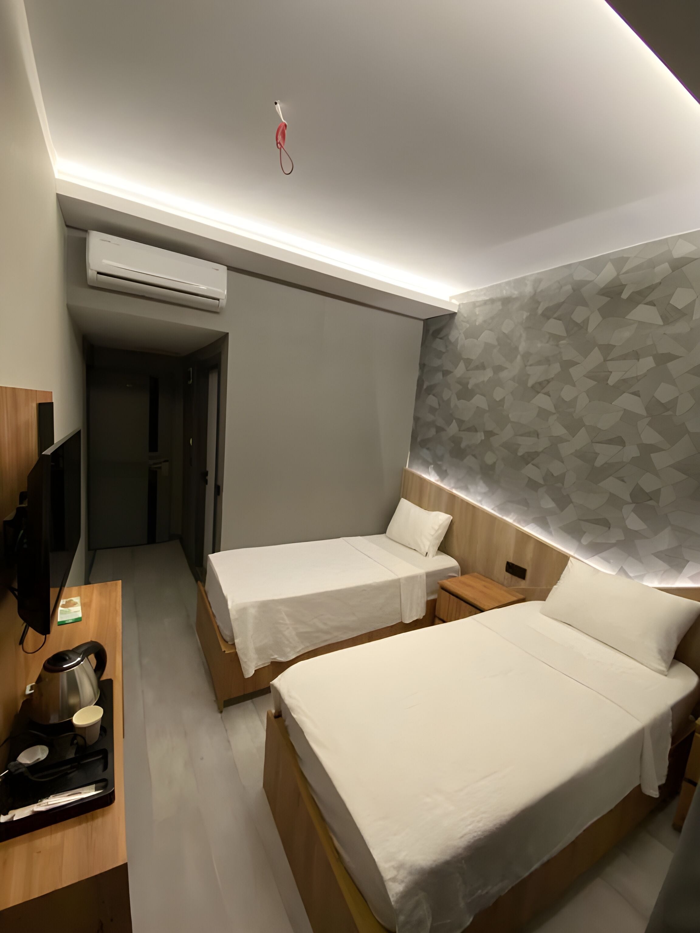 Habitación de hotel con dos camas individuales, un escritorio de madera con hervidor, televisión de pantalla plana y aire acondicionado de pared.