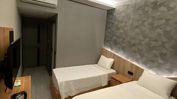 Habitación de hotel con dos camas individuales, un escritorio de madera con hervidor, televisión de pantalla plana y aire acondicionado de pared.