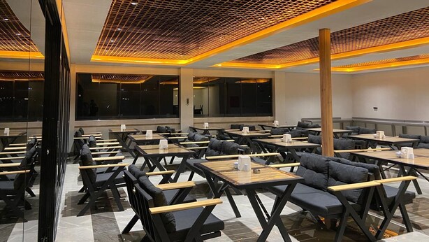 A modern dining area with tables and chairs, a patterned ceiling, and large windows. - OTEL ORTADOĞU (Sanliurfa)