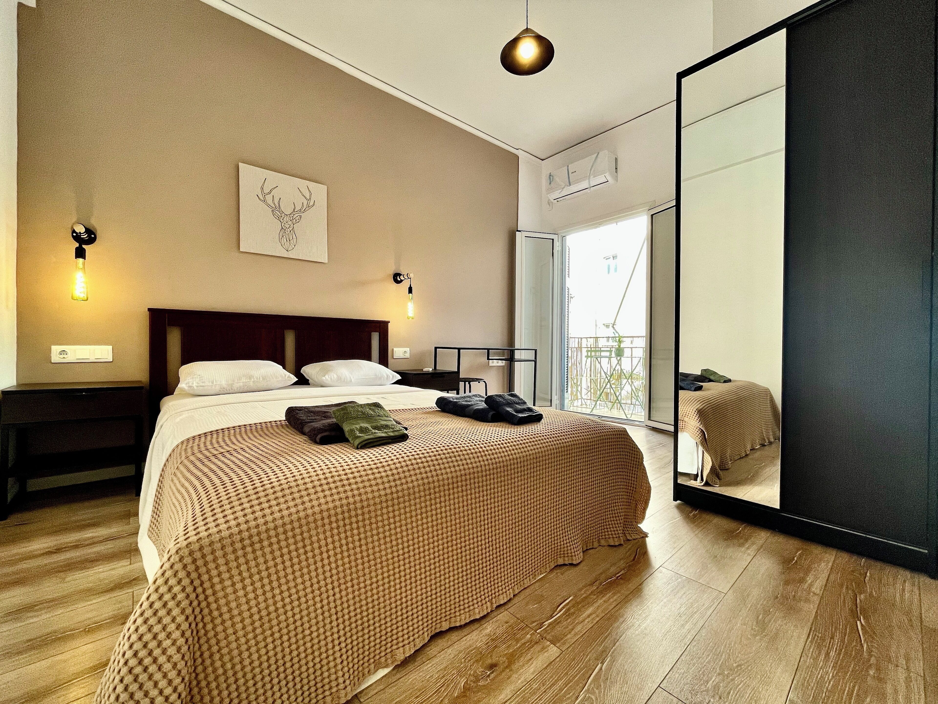 Una camera d'albergo moderna con un letto grande, una testiera in legno, una lampada fissata al muro e un lampadario, oltre a un ampio specchio.
