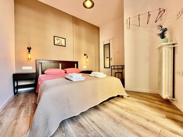Un lit bien fait, avec une literie rose et blanche, une tête de lit en bois et une table de chevet avec une lampe.