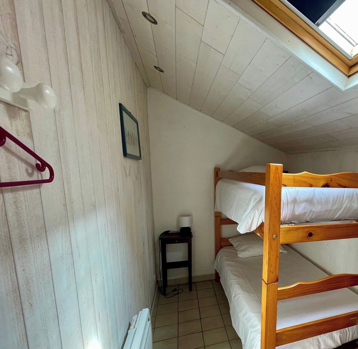 A bunk bed room with a skylight, a small table with a lamp, and a framed picture on the wall.