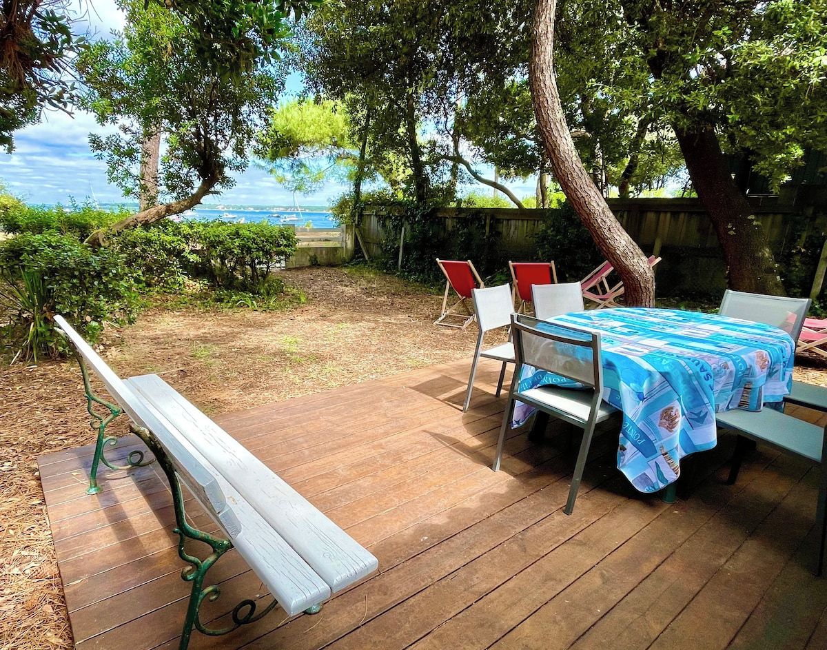 Um deck de madeira com uma mesa e cadeiras, um banco e vista para o mar.