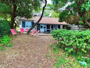 A house with a tiled roof, a covered porch, and a small garden area with red lounge chairs. - Small bay view house in 1st line - Mimbeau A0392 (Lège-Cap-Ferret)