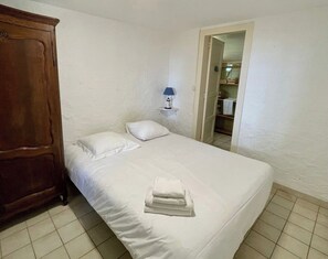 A single bed with white linens, a wooden wardrobe, and a nightstand with a lamp.
