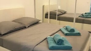 Una cama individual con colchón y almohadas grises, una toalla doblada y un armario con espejo.