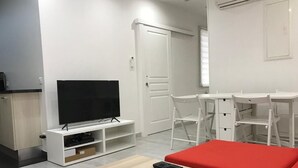 Una sala de estar moderna con un televisor de pantalla plana sobre un soporte blanco, un sofá rojo, una mesa de centro de madera y sillas blancas.
