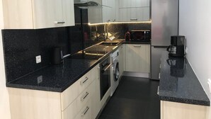 Una cocina moderna con encimera negra, electrodomésticos de acero inoxidable y armarios de madera clara.