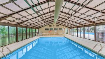 An indoor swimming pool with a metal roof, clear glass walls, and a view of the outside.