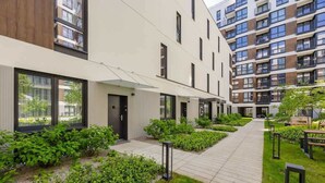 A modern apartment building with a clean, minimalist design, featuring large windows and a well-maintained garden area.