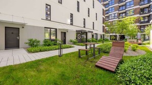A modern building with a flat roof, multiple windows, and a well-maintained garden area with benches and a wooden deck.