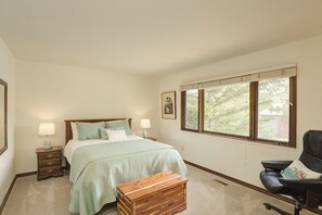 Une chambre à coucher avec un lit, des lampes de chevet, une commode en bois, une chaise et une fenêtre donnant sur des arbres.