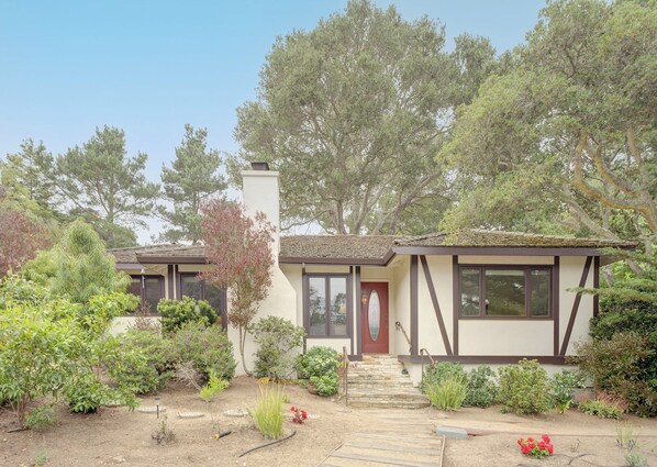 Une maison à deux étages avec un jardin à l’avant, une porte rouge et une cheminée.