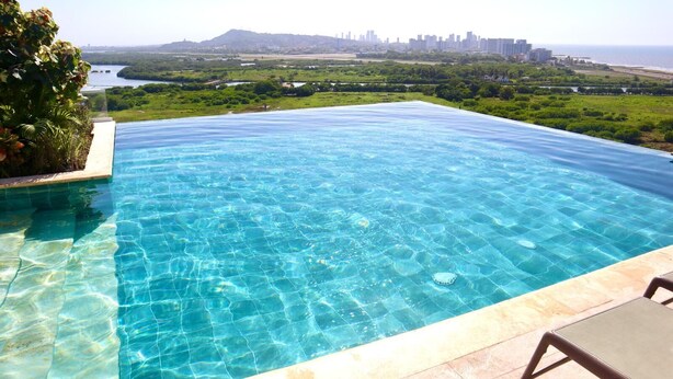 Uma piscina infinita azul cristalina com um horizonte urbano ao fundo.
