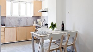A modern kitchen with wooden cabinets, a white countertop, and a dining area with a table and chairs. - Mini Suites 2 (Chania)