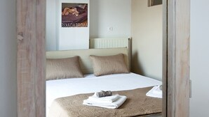 A neatly made bed with a patterned bedspread and two pillows, a rolled towel, and a folded towel on the bed. - Mini Suites 2 (Chania)