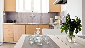 A modern kitchen with wooden cabinets, a marble countertop, and a dining area with a table set for four. - Mini Suites 2 (Chania)