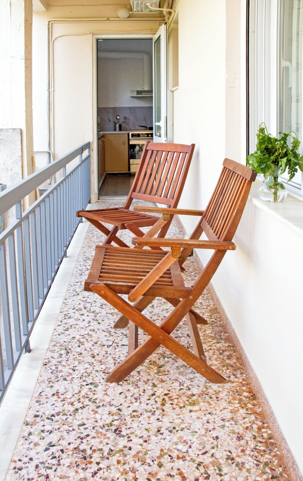 A balcony with two wooden chairs and a potted plant.