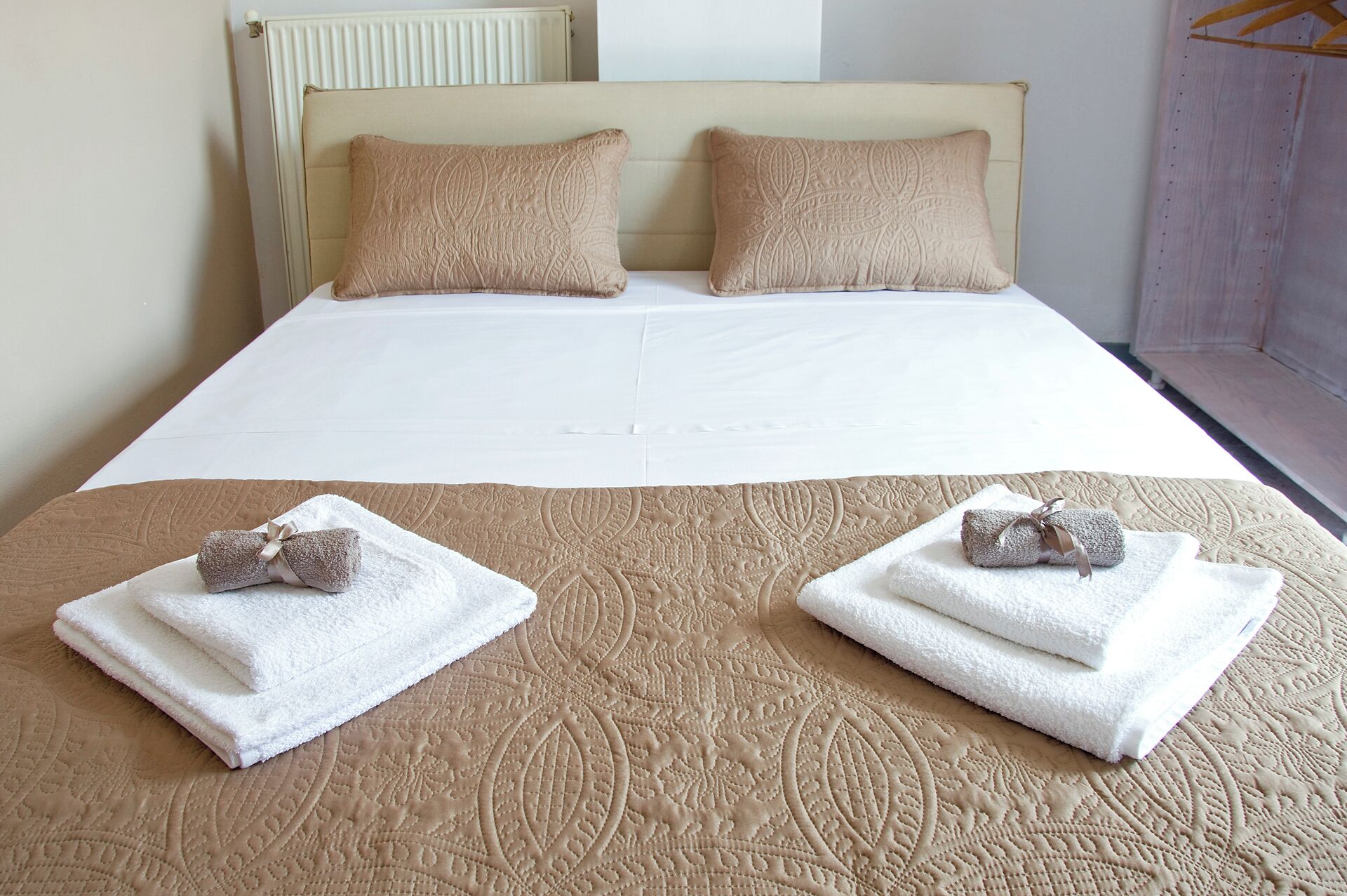 A neatly made bed with a beige quilt, two pillows, and two towels with bows on the bed.