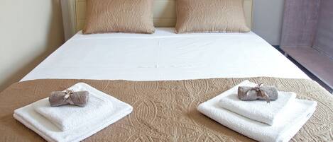 A neatly made bed with a beige quilt, two pillows, and two towels with bows on the bed.