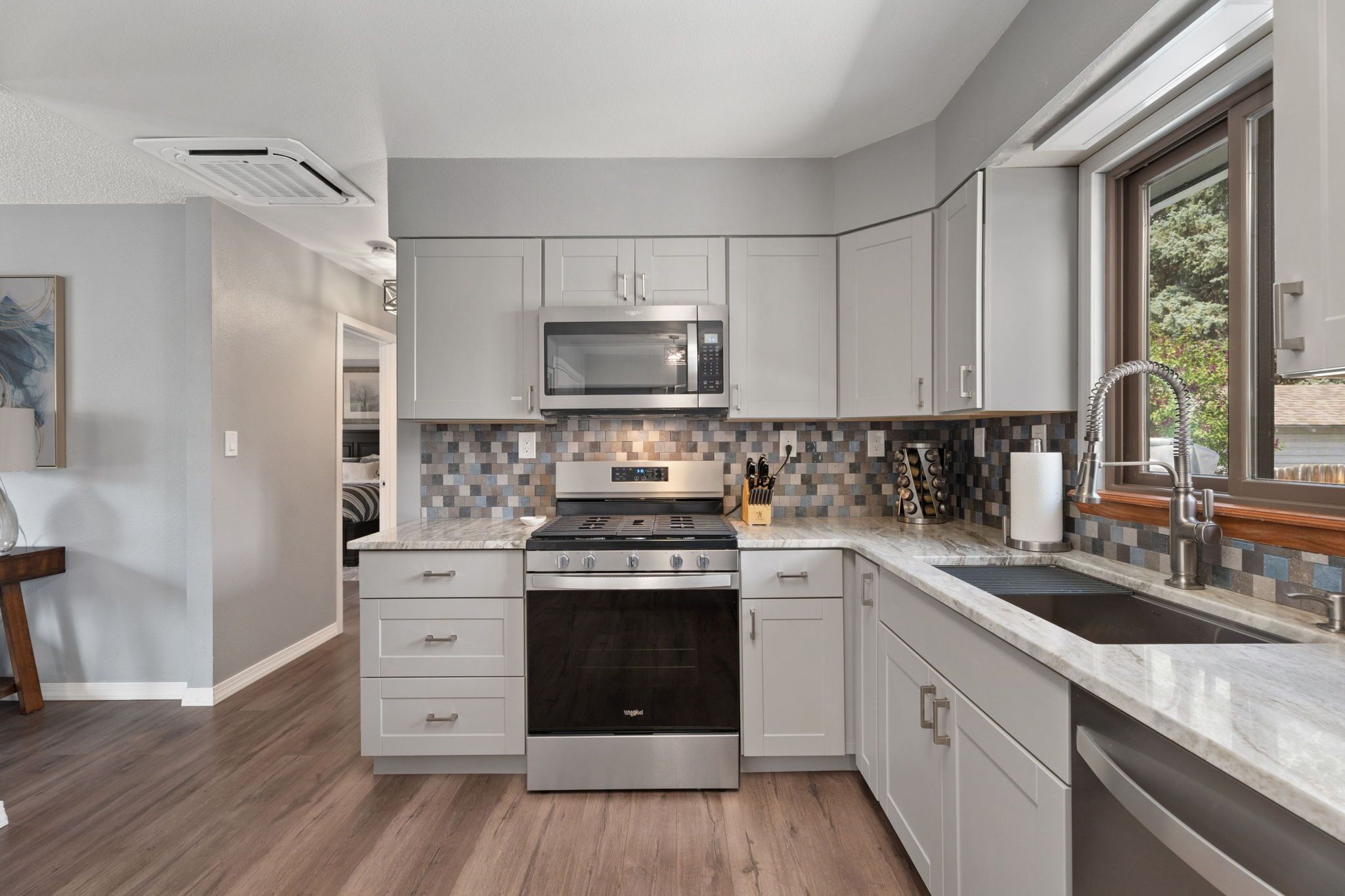 A modern kitchen with grey cabinets, a stainless steel stove, a microwave, and a large window providing natural light.