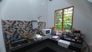 A compact kitchen with a microwave, stove, sink, and window with a view of greenery.