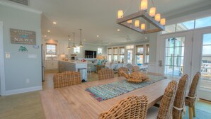 A spacious kitchen with a central island, a dining area with wicker chairs, and a large window providing natural light. - Discover beachfront bliss at Starboard Side, Oak Island's spacious 4-bedroom retreat. (Oak Island)