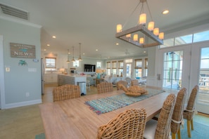 A spacious kitchen with a central island, a dining area with wicker chairs, and a large window providing natural light.