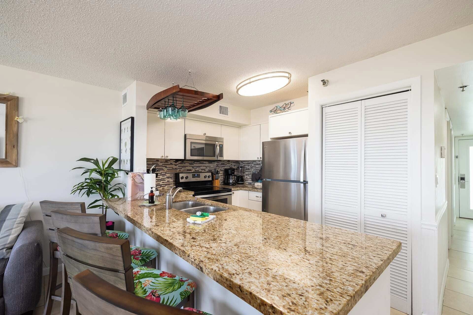A kitchen with granite countertops, stainless steel appliances, and a bar area with bar stools.