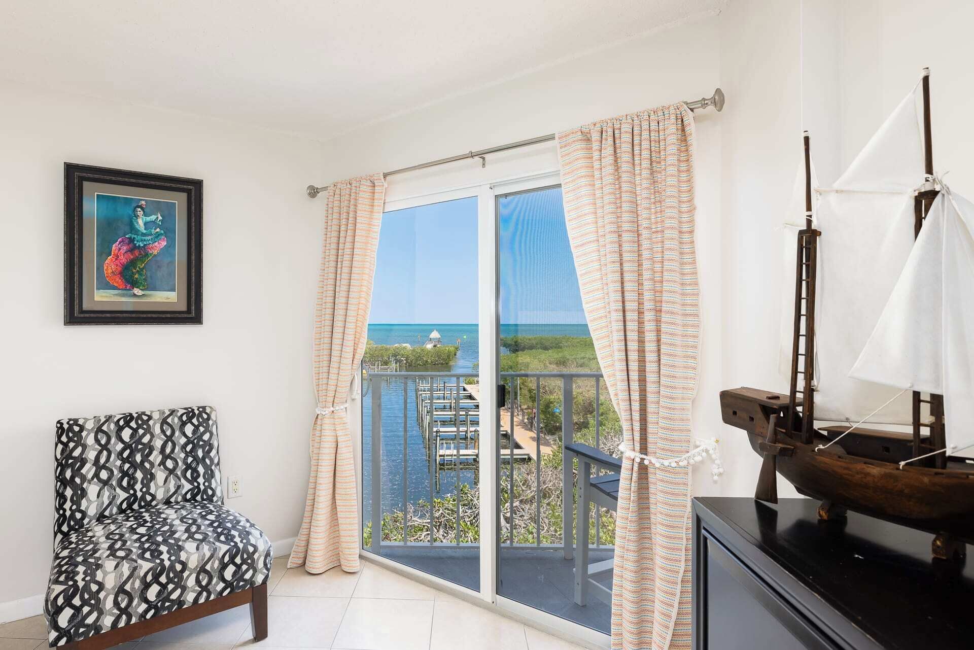 A room with a balcony, a framed artwork, a patterned chair, and a sailboat model.