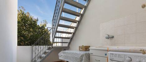 Un área de lavandería con lavadora, una mesa con mantel y una escalera que lleva a un espacio exterior.