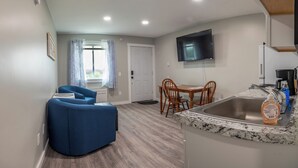 A compact living space with a dining area, a kitchen with a granite countertop, and a flat-screen TV mounted on the wall. - Beautiful Apartments in Thorsen Road Maine (Hancock)