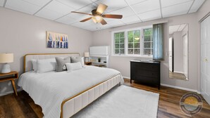 Ein Schlafzimmer mit Bett, Deckenventilator, Fenster, Kommode und Nachttisch.