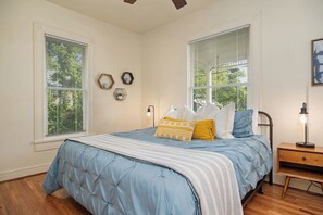 A bedroom with a bed, two windows, a bedside table, and a lamp.