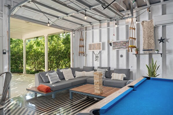 A covered outdoor area with a pool table, sofas, and a wooden table.