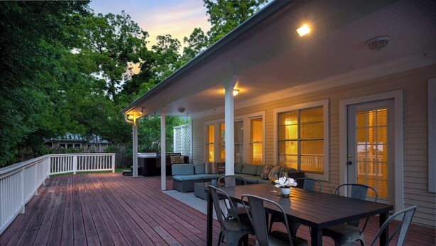Une terrasse en bois avec une table et des chaises, un espace salon couvert et une rambarde blanche.