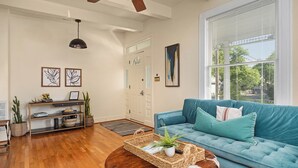 Un salon avec un canapé bleu, une table basse en bois, un ventilateur de plafond et une grande fenêtre avec des stores.