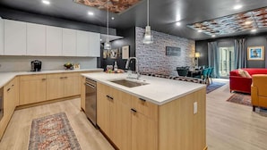 A modern kitchen with a central island, a dining area with a red sofa, and a living room with a yellow armchair. - Hyve-Prohibition Parlor-Pool & Gym-Mins 2 Broadway (Nashville)