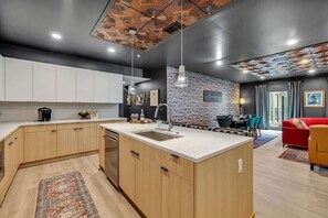 A modern kitchen with a central island, a dining area with a red sofa, and a living room with a yellow armchair.