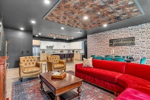 Uma sala de estar moderna com um sofá vermelho, poltronas de couro, uma mesa de centro de madeira e uma cozinha ao fundo.