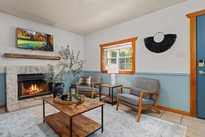 Una sala de estar con chimenea, un televisor montado encima, un ventanal con vistas y una puerta con marco azul.