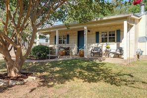 A single-story house with a covered porch, a front door, and a small front yard with a tree and potted plants. - Orange Blossom Hideaway - Hot Tub & Fire Pit (Fredericksburg)