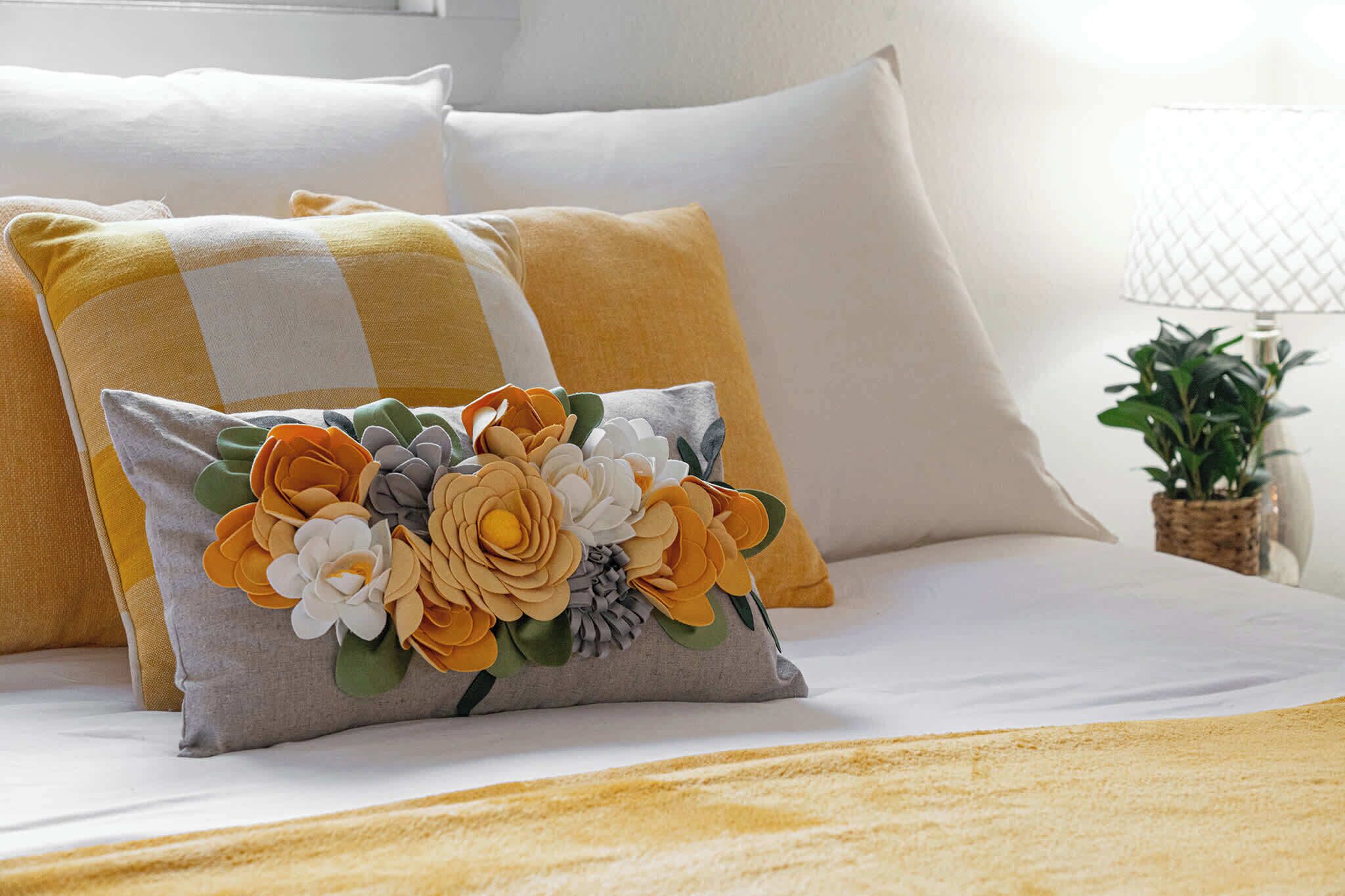 A bed with white bedding, a decorative pillow with a floral design, and a lamp with a white shade.
