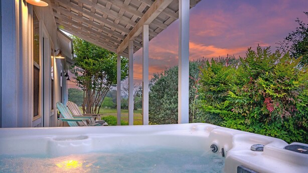 Un jacuzzi bajo una pérgola con vistas a un jardín y al atardecer.