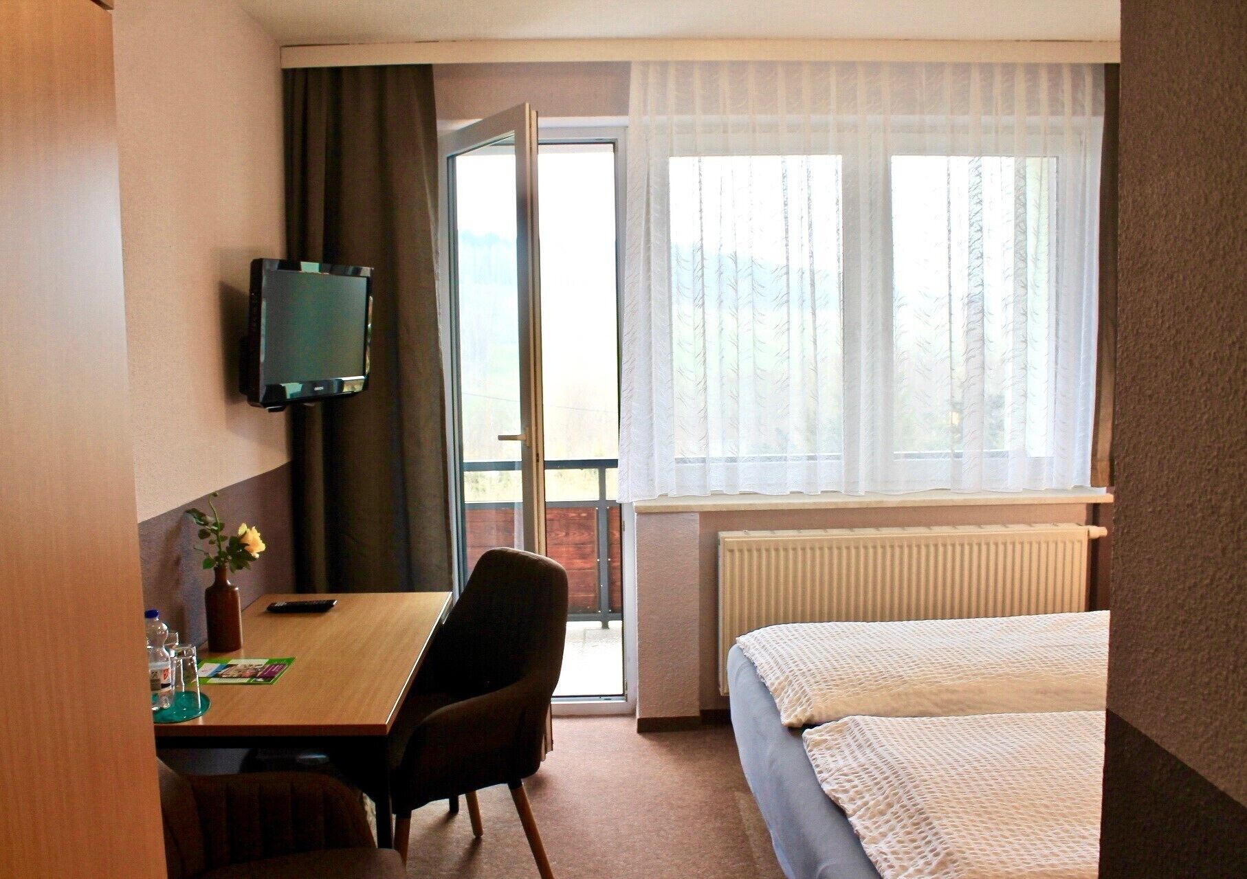 Une chambre d’hôtel comprenant un lit, un bureau avec une chaise, une télévision et une fenêtre avec des rideaux.