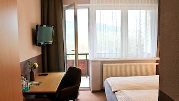Ein Hotelzimmer mit Bett, Schreibtisch mit Stuhl, Fernseher und einem Fenster mit Vorhängen.