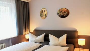 A hotel room with a bed, two wall art pieces, a window with curtains, and a bedside lamp.