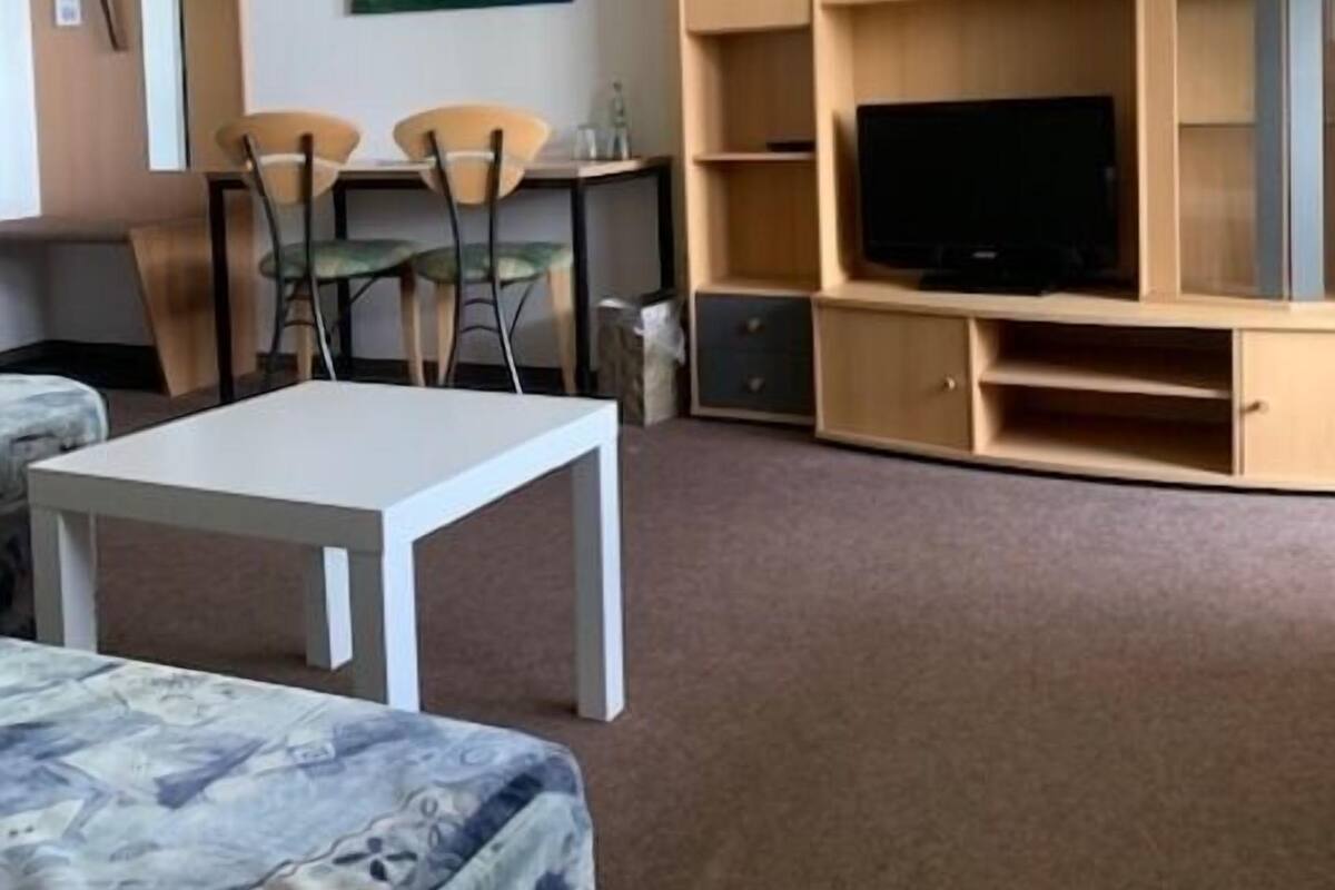 A compact living room with a flat-screen TV, a dining table with chairs, and a painting on the wall.