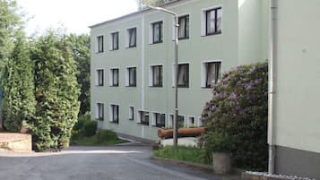 Un edificio de varios pisos con fachada verde claro, múltiples ventanas y un pequeño jardín con arbustos y flores.